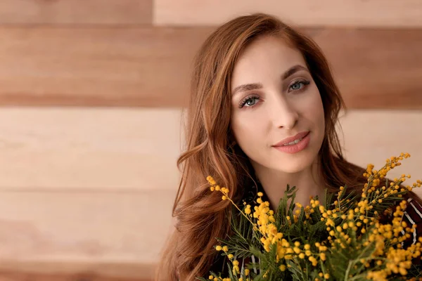 Beautiful young woman with bouquet of mimosa flowers on wooden background