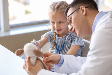 Küçük kız nasıl klinikte stetoskop kullanılacağını gösteren oyuncak çocuk doktoru