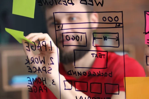 Young IT designer with drawn wireframe on transparent board