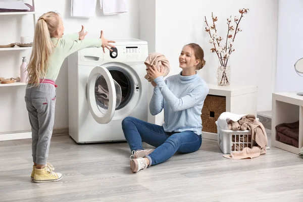 Mujer joven y su hija pequeña jugando mientras lavan la ropa en casa — Foto de Stock