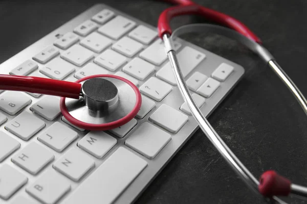 Estetoscópio e teclado do computador em fundo cinza, close-up. Conceito de consulta médica online — Fotografia de Stock