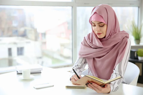 Mujer musulmana joven escribiendo en cuaderno en la mesa — Foto de Stock