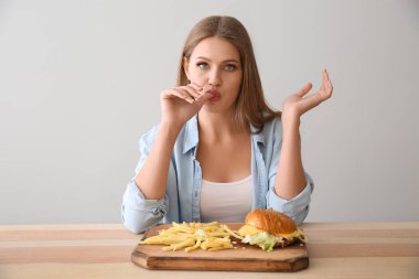 Genç kadın lezzetli burger patates kızartması ile masada yemek