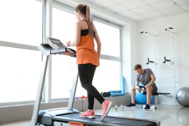 Spor salonundaki koşu bandında antrenman yapan genç bir kadın.