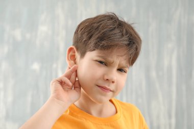 Gri arka planda işitme sorunu olan küçük çocuk