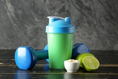 Şişe protein sallamak ahşap masa üzerinde dumbbells ile