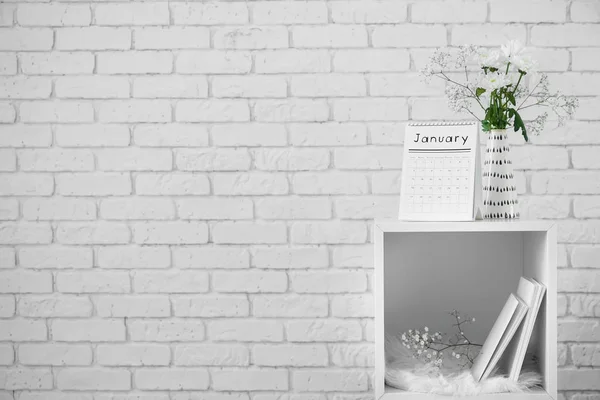 Flip calendar and vase with bouquet of flowers on shelf unit against white brick wall — Stock Photo, Image