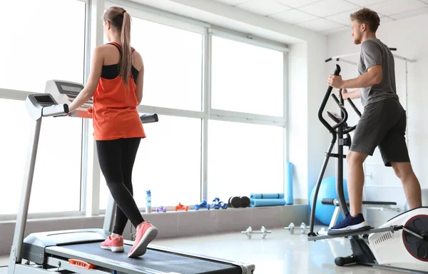 Sporty young people training on machines in gym — Stock Photo, Image