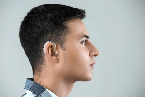 Young man with hearing aid on grey background — Stock Photo, Image