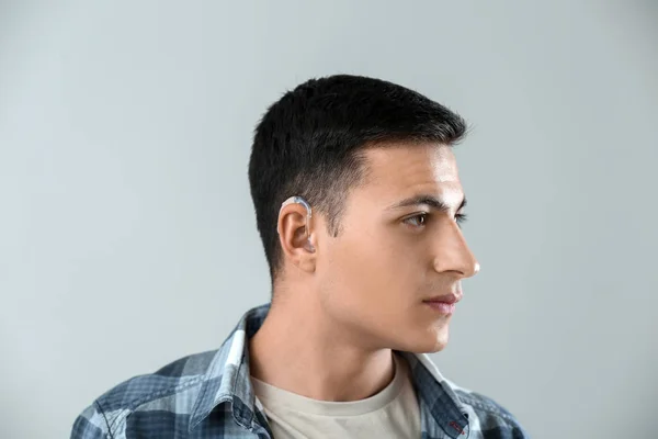 Hombre joven con audífono sobre fondo gris — Foto de Stock