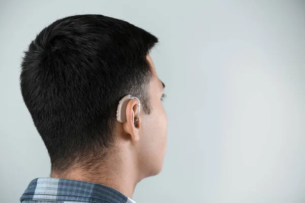 Hombre joven con audífono sobre fondo gris —  Fotos de Stock