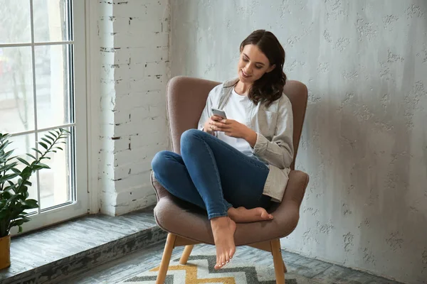 Mulher bonita com telefone celular descansando em casa — Fotografia de Stock