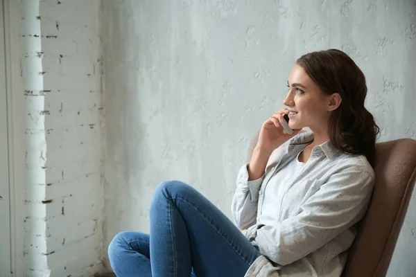 Beautiful young woman talking by mobile phone at home — Stock Photo, Image