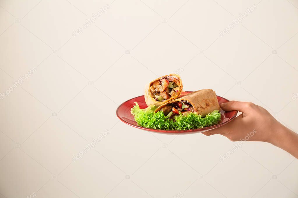 Female hand holding plate with tasty doner kebab on light background