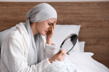 Desperate woman after chemotherapy looking in mirror at home clipart