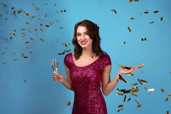 Gyönyörű fiatal nő, pohár pezsgőt és a csökkenő konfetti színes háttérrel — Stock Fotó