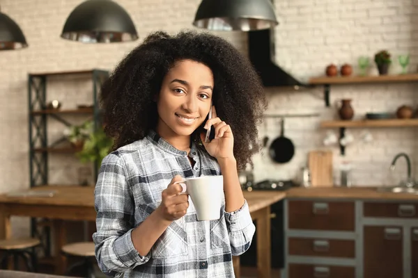 Bella donna afro-americana che beve caffè e parla per telefono a casa — Foto Stock