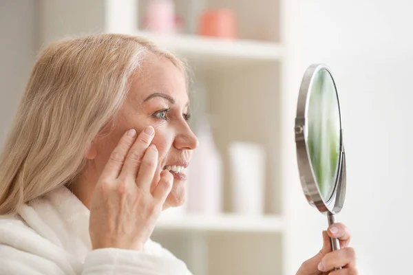 Rijpe vrouw met een gezonde huid op zoek in spiegel — Stockfoto