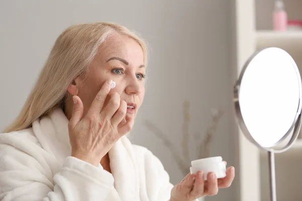 Mulher madura aplicando creme facial em casa — Fotografia de Stock