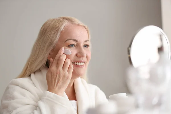 Mujer madura aplicando crema facial en casa — Foto de Stock