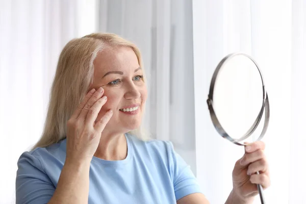 Reife Frau mit gesunder Haut schaut zu Hause in den Spiegel — Stockfoto