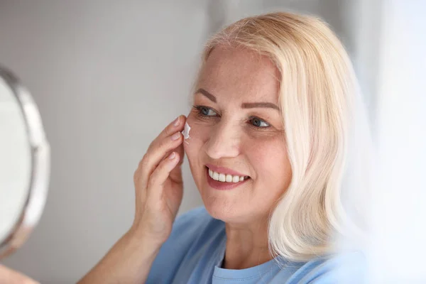 Mujer madura aplicando crema facial en casa — Foto de Stock