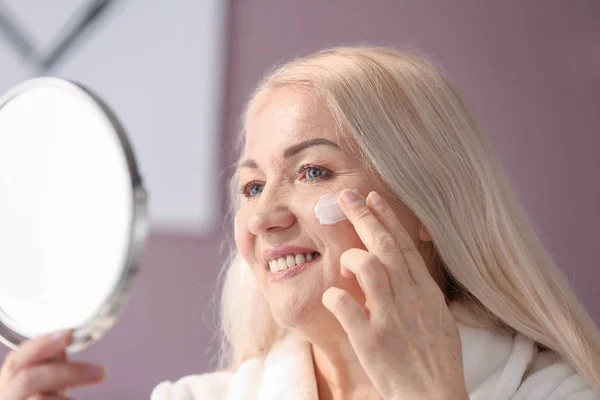 Rijpe vrouw toe te passen gezichtscrème thuis — Stockfoto