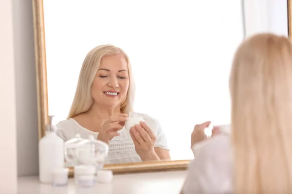 Mulher madura aplicando creme facial em casa — Fotografia de Stock