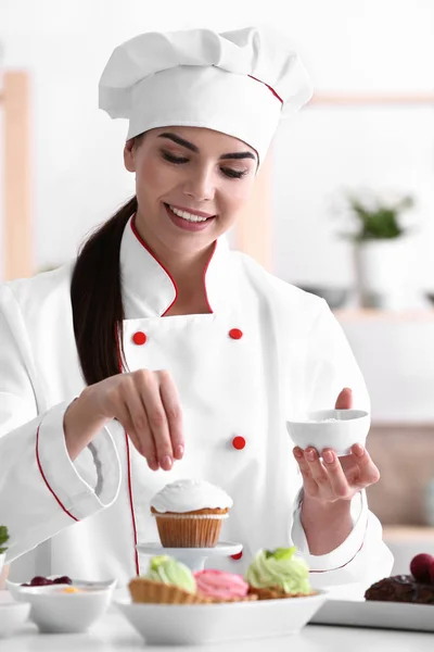 Young female confectioner decorating cupcake in kitchen