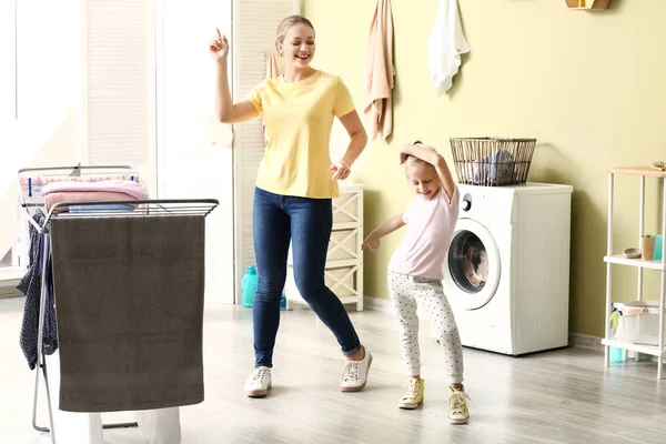 Mujer joven y su hija pequeña bailando mientras lavan la ropa en casa — Foto de Stock