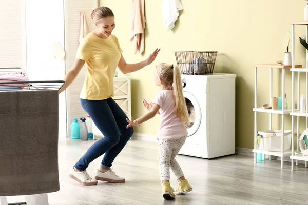 Mujer joven y su hija pequeña bailando mientras lavan la ropa en casa — Foto de Stock