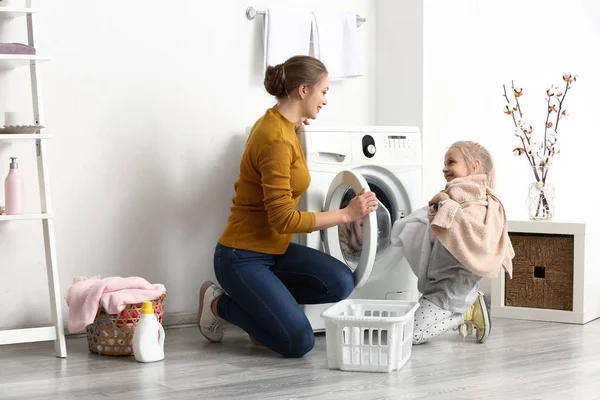 Mujer joven y su hija pequeña haciendo la colada en casa — Foto de Stock