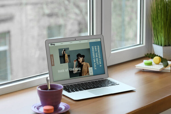 Laptop with open page of fashion blog and cup of coffee on window sill