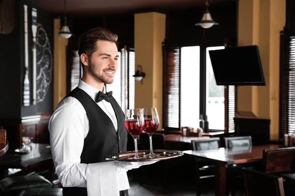 Young male waiter with glasses of wine in restaurant — Stock Photo, Image
