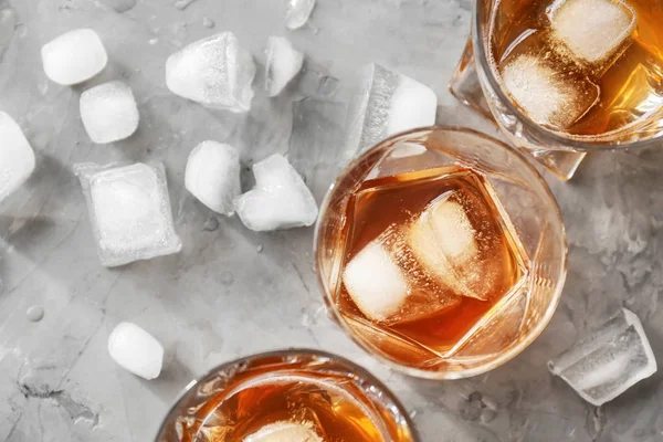 Glasses of cold whiskey with ice on grey background — Stock Photo, Image