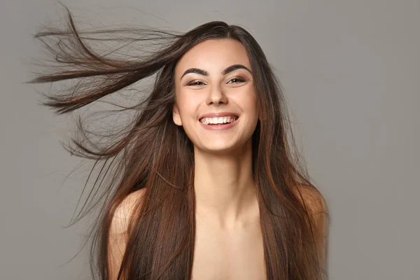 Portrait of beautiful young woman with healthy long hair on grey background — Stock Photo, Image