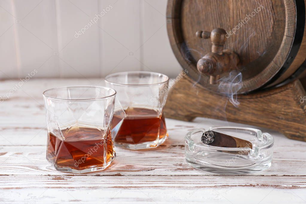 Glasses of cold whiskey with cigar on white table