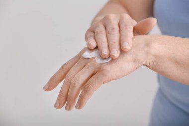 Olgun kadın gri arka planda el kremi uygulayarak, çekim