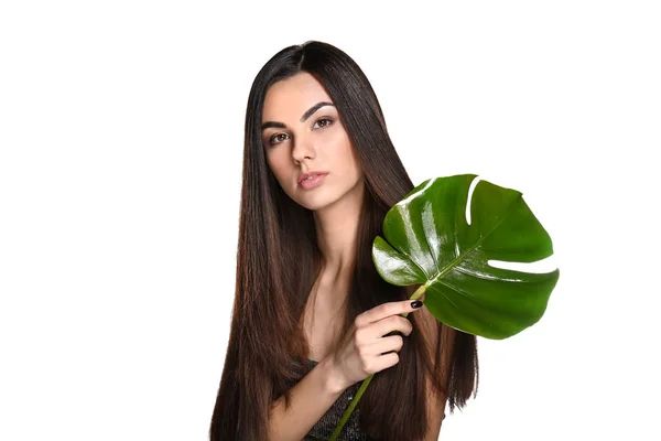 Portrait of beautiful young woman with healthy long hair holding tropical leaf on white background — Stock Photo, Image