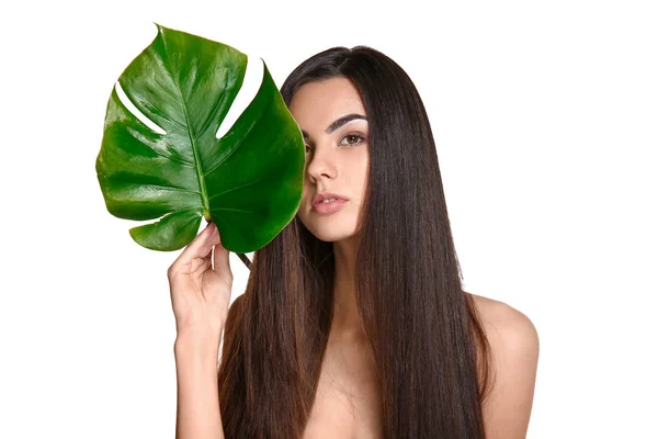 Portrait of beautiful young woman with healthy long hair holding tropical leaf on white background — Stock Photo, Image