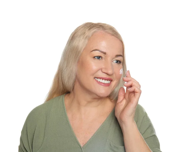 Mature woman applying facial cream on white background — Stock Photo, Image