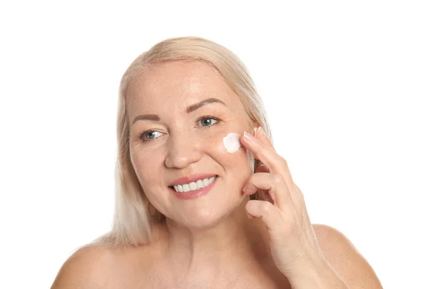 Mujer madura aplicando crema facial sobre fondo blanco — Foto de Stock