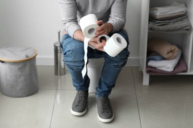 Man with rolls of paper sitting on toilet bowl at home