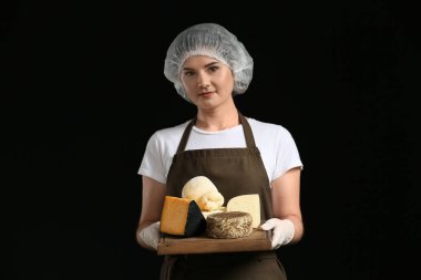 Woman holding board with assortment of tasty cheese on dark background clipart
