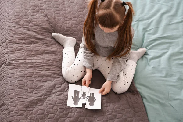 Sad little girl with torn picture of family sitting on bed. Concept of divorce — Stock Photo, Image