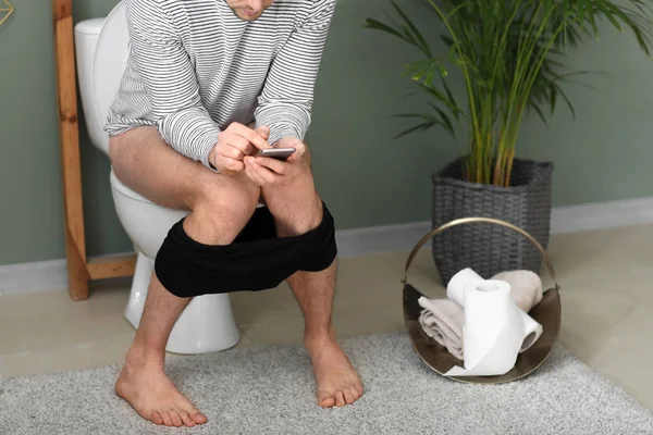 Homem com telefone celular sentado no vaso sanitário em casa — Fotografia de Stock