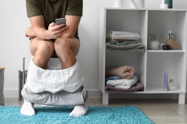 Homem com telefone celular sentado no vaso sanitário em casa — Fotografia de Stock