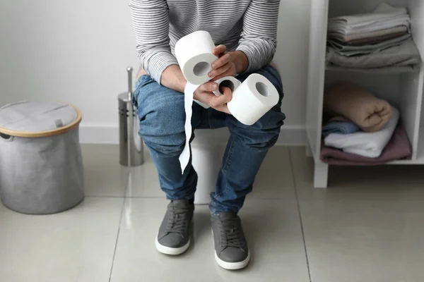 Homem com rolos de papel sentado no vaso sanitário em casa — Fotografia de Stock