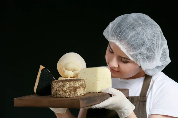 Женщина держит доску с ассортиментом вкусного сыра на темном фоне — стоковое фото