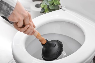 Young woman using plunger to unclog a toilet bowl clipart